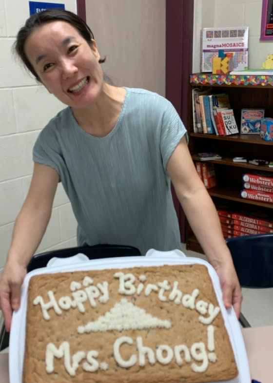 Mrs. Chong holding a cookie cake iced with “Happy Birthday Mrs. Chong!” and a bell curve