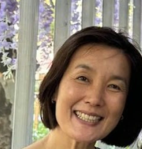 Mrs. Chong smiling under a wisteria arbor